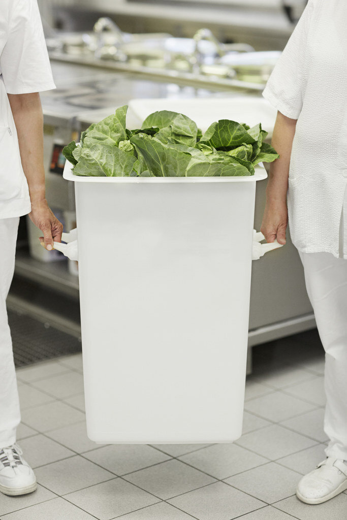 Mit Salat gefüllter Großbehälter weiß getragen an seitlichen Henkeln