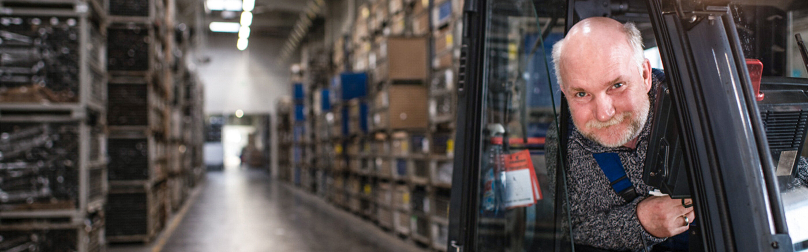 Warehouse employee looks out of a forklift in a friendly manner