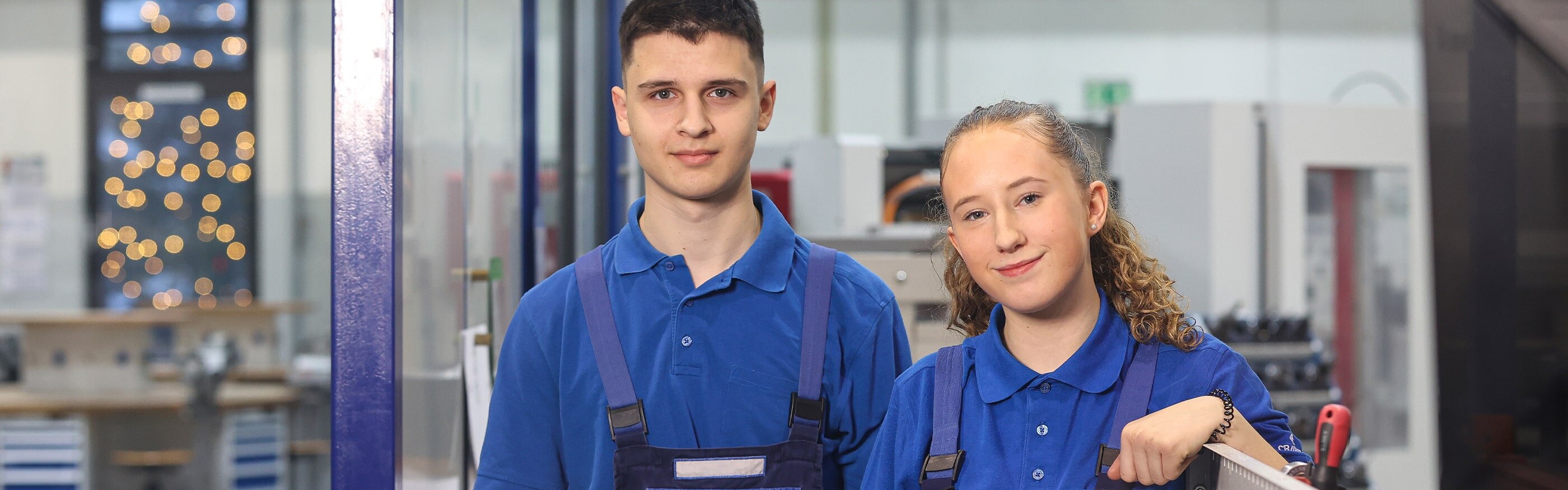 Zwei Auszubildende in blauer Arbeitskleidung schauen freundlich