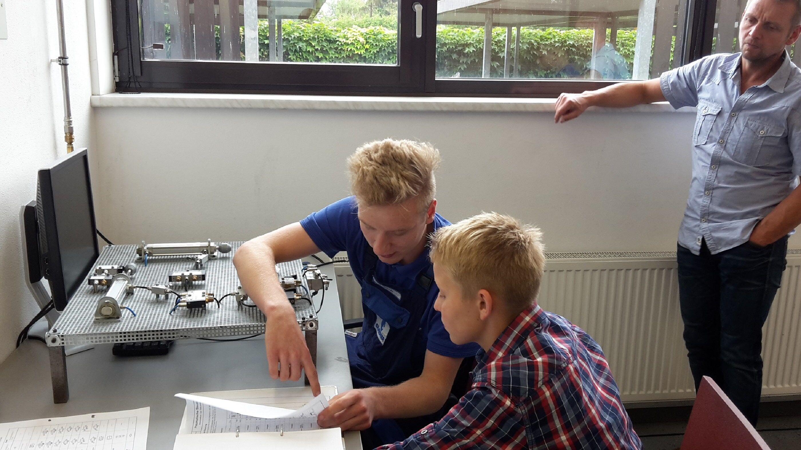 Auszubildender erklärt einem Schüler den Aufbau einer Pneumatiksteuerung