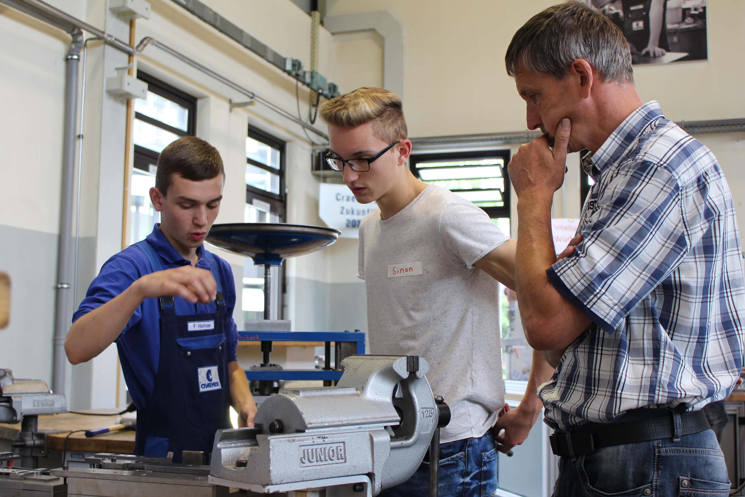 Auszubildender erklärt Schüler und dessen Vater den Aufbau eines Stanzwerkzeugs