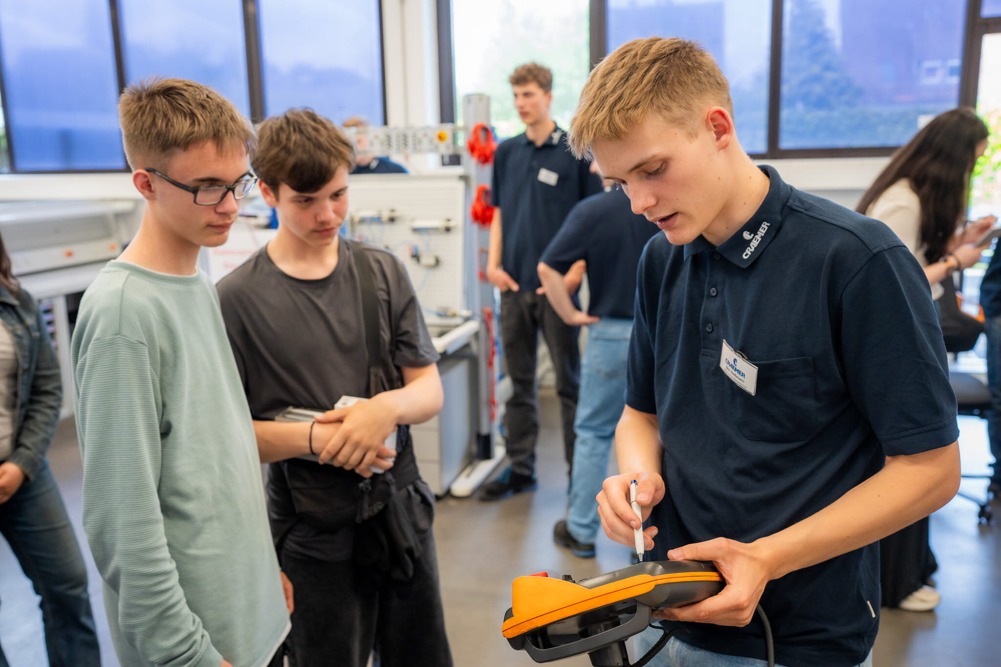 Julian Huwe (l.) und Jonas Pinzke lassen sich von Ben Heißmann (r.), Elektroniker-Azubi für Betriebstechnik im 1. Lehrjahr, die Programmierung eines Industrieroboters erklären