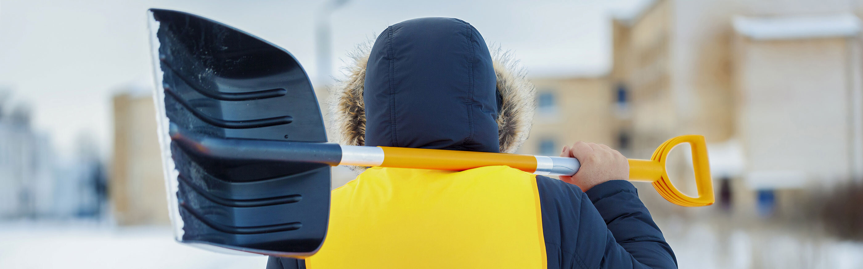 Person von hinten mit Schneeschaufel über der Schulter